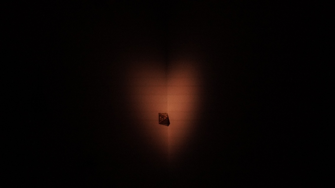 Light animation still — a small diamond-shaped object in the corner of two walls, lit by a warm amber light radiating from the meeting point of the surfaces.