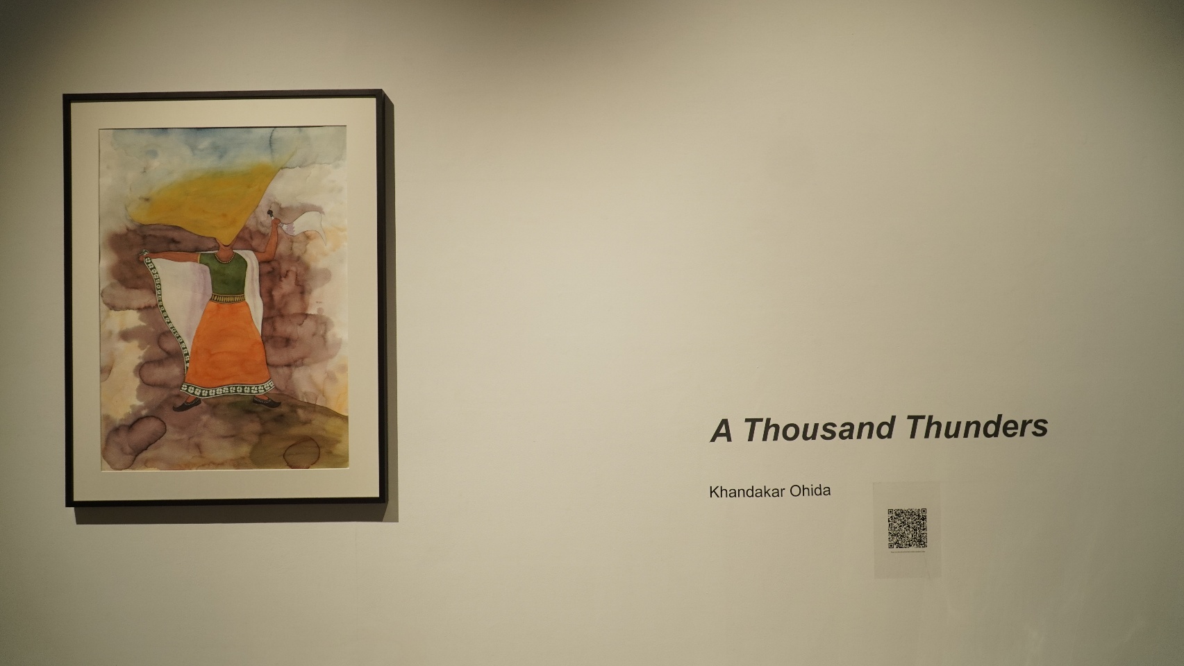Exhibition entrance view of A Thousand Thunders, Project 88, Mumbai, 2024. A framed watercolour painting of a headless woman in an orange skirt and green top holding a white flag against stormy dark clouds hangs on the white gallery wall to the left, with the exhibition title 'A Thousand Thunders' and the artist's name lettered on the wall to the right alongside a QR code.