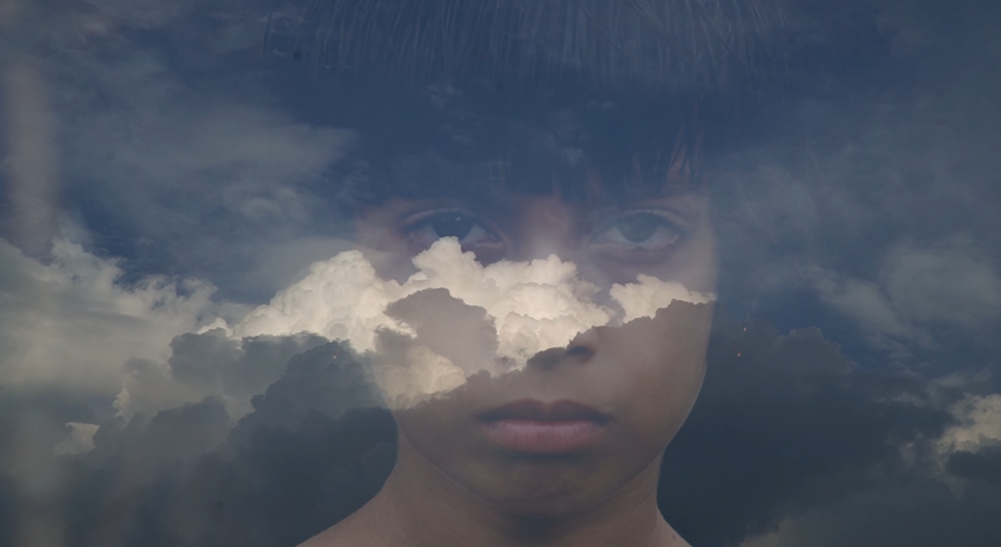 Still from The Last Dream I Saw — a double-exposure composite of a woman's face merged with a dramatic cloudy sky, suggesting dreams and interiority.