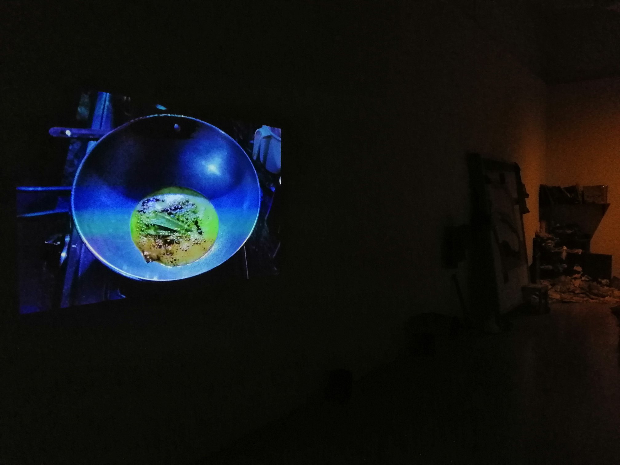 Video installation projection view on wall, Serendipity Art Festival, Panjim, Goa, 2019 — a glowing image of a wok or cooking vessel projected in a darkened gallery space.