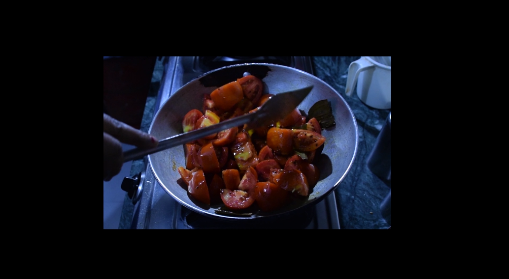 Video still from Ungraceful Melody — a close-up of cooked food in a blackened wok or pan, evoking the domestic labour of cooking.