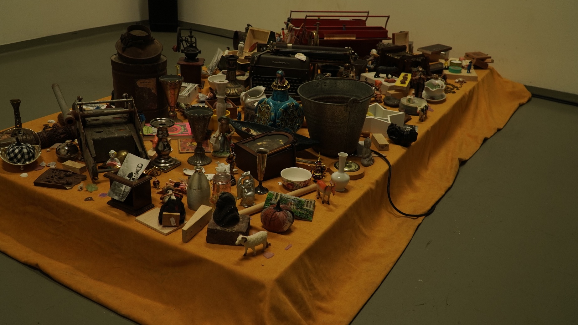 Objects installation — a wide overhead view of the full collection of found objects arranged on an orange-draped table at Jan Van Eyck Academie, gathered from the Netherlands and UAE.