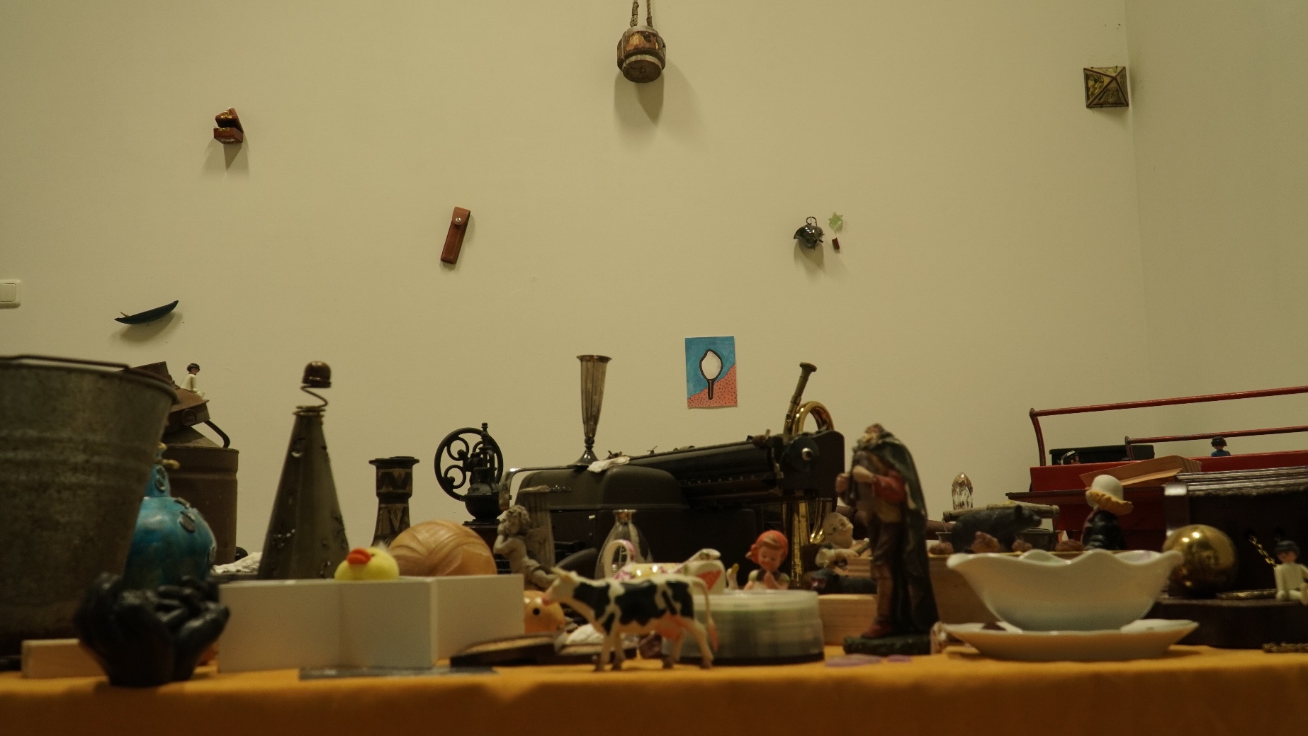 Objects installation — a mid-range view of the collection showing diverse objects on the table alongside smaller items pinned directly to the gallery wall above, used for the light animation.